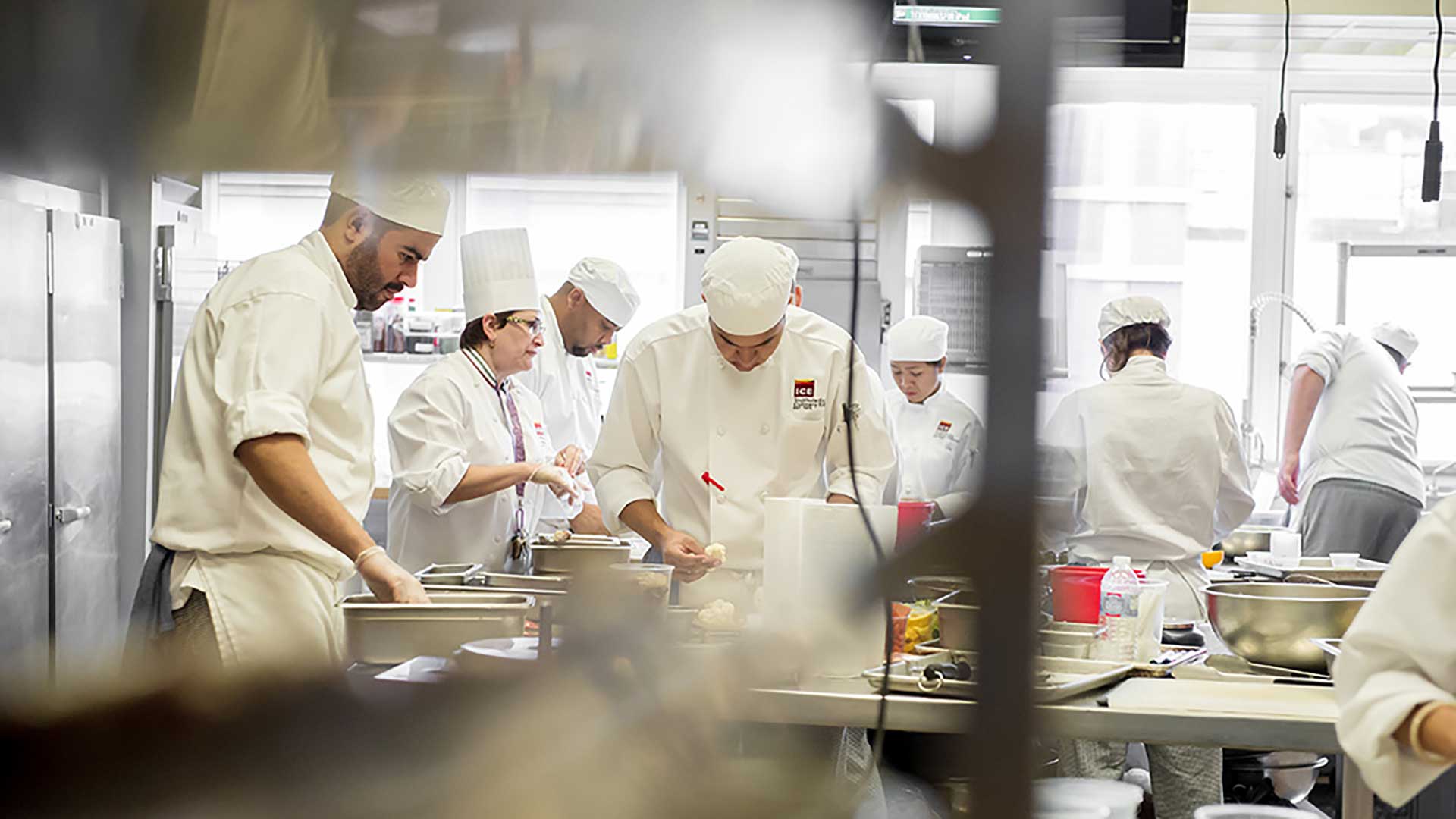 Multiple people in white uniforms working in a commercial kitchen